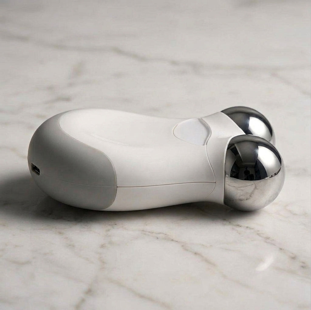 A handheld beauty device with a white and gray body and two polished silver metal spheres, resting on a white marble surface.